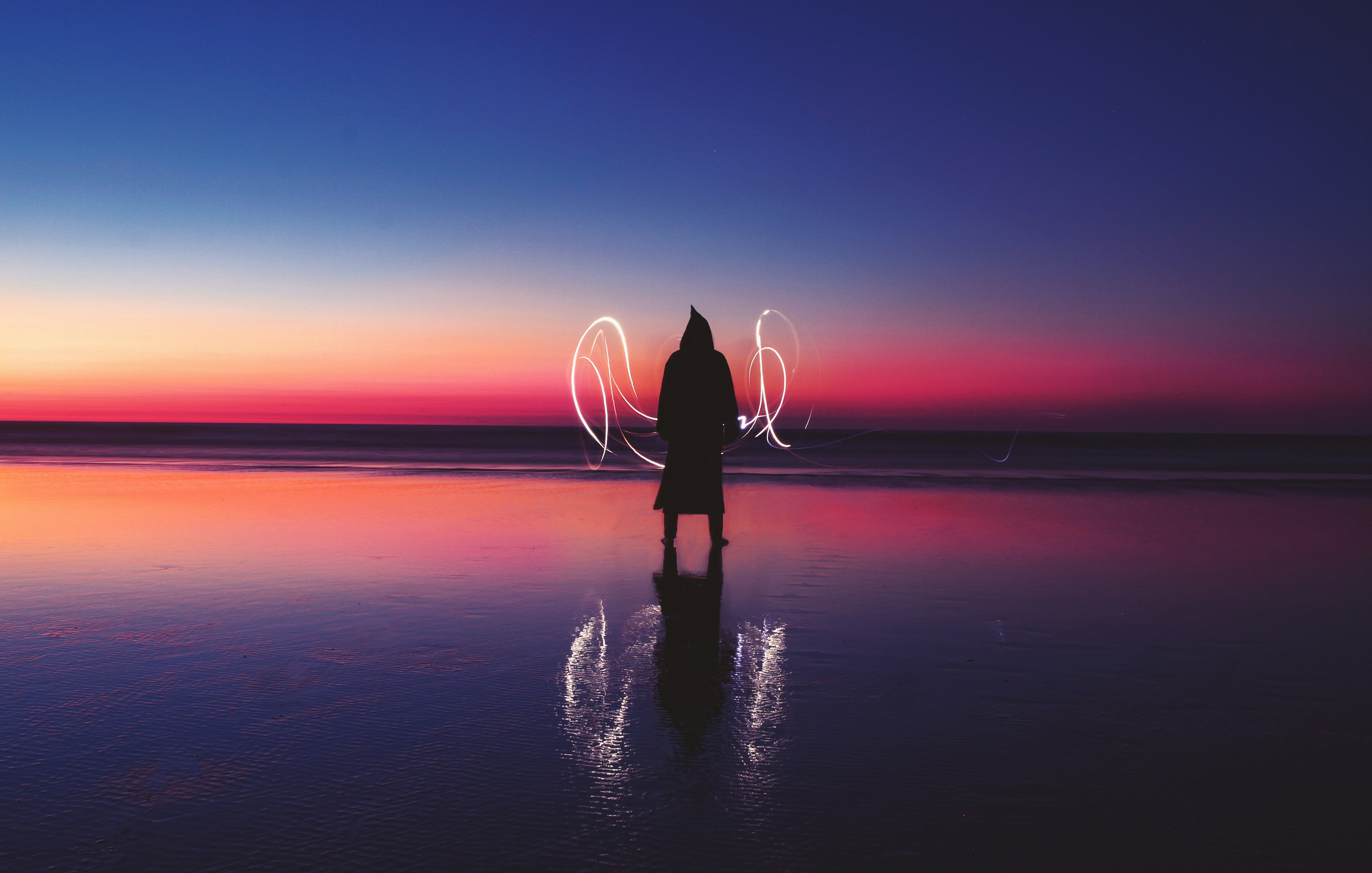 silhouette of person standing on body of water with light wave